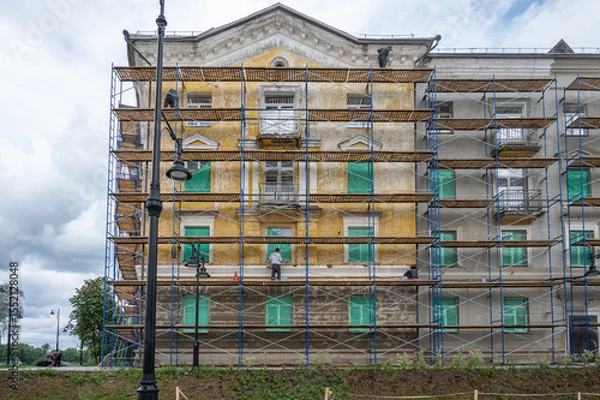 Fototapeta An old building in scaffolding during renovation and painting of the facade.
