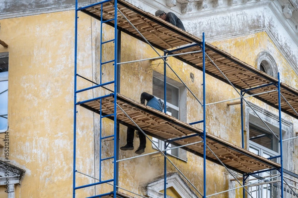 Fototapeta An old building in scaffolding during renovation and painting of the facade.