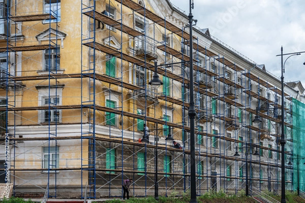 Fototapeta An old building in scaffolding during renovation and painting of the facade.