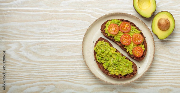 Obraz Two slices of whole rye bread are topped with mashed avocado, green peas, cherry tomatoes, and sesame seeds, a healthy and vibrant breakfast or snack option
