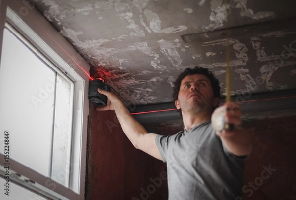 Fototapeta A young man uses a laser level to install windows.