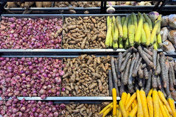 Fototapeta Assorted fresh vegetables on display at a local market, including turmeric, shallots, black carrots, yellow carrots and green carrots. Colorful and neatly arranged root vegetables for sale