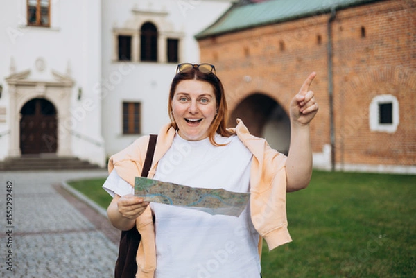 Obraz Happy young woman with map in old town. Holidays and tourism concept. Female tourist searching direction on location map while traveling abroad in summer