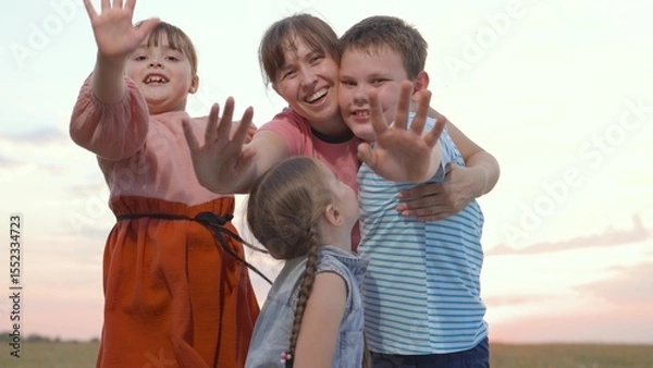 Obraz Mother, children play in park. Happy family concept. Mom, Children happily wave their hands, look at camera. Happy child laughing in park. Faces of child, children emotion of happiness at sunset sky
