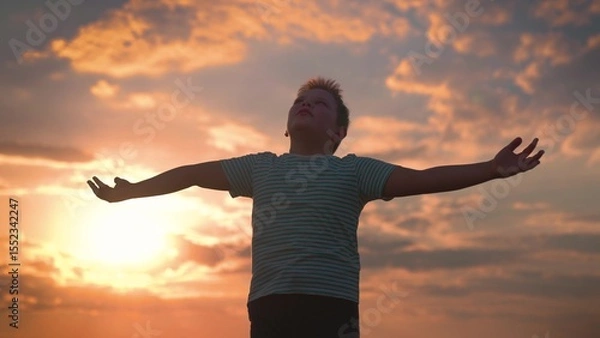 Obraz Child plays in park against sky. Little boy prays against background of sky and sun. Child raised his hands to sky in park at sunset, true faith. Religion and god, childhood dreams. Happy family