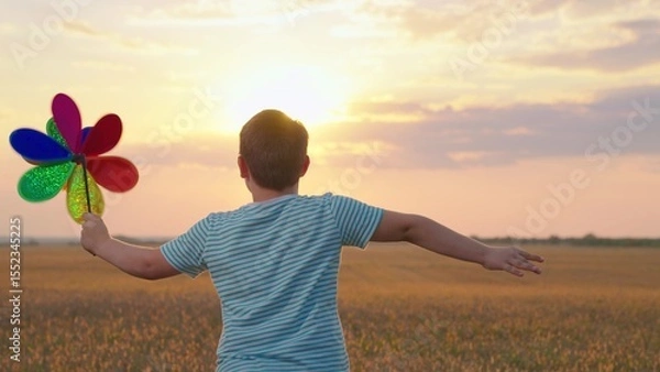 Obraz Family vacation in nature, sky, Happy kid plays with toy pinwheel outdoors in spring park in sunshine. Childhood, children. Little boy runs with toy wind turbine in his hand on summer field at sunset.