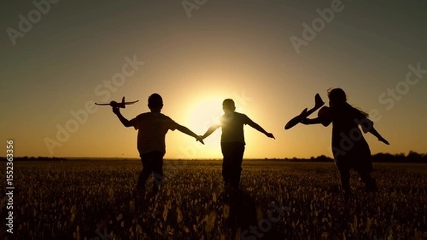 Obraz Children play with toy plane. Happy children run with toy plane across field at sunset. Boy, girl wants to become pilot, astronaut. Teenager dreams of flying, becoming pilot. Silhouette