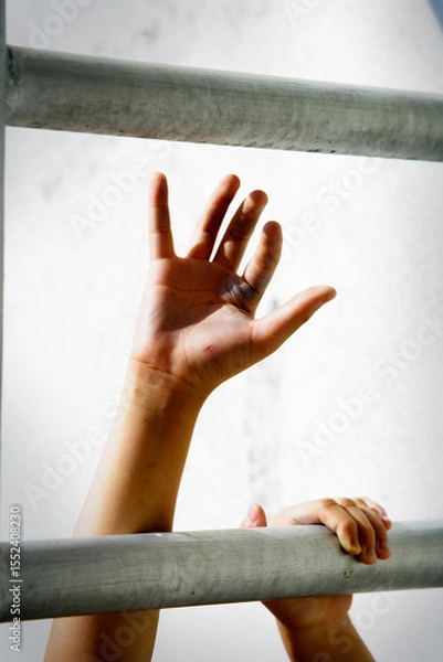 Fototapeta Hands Reaching for Freedom Through Metal Bars in Soft Light