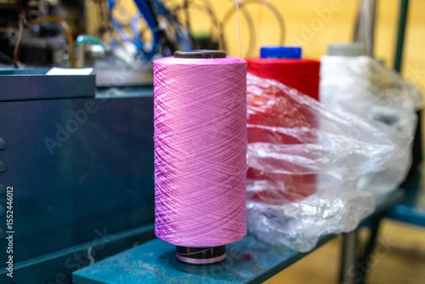 Fototapeta Pink yarn spool with red and white threads in a textile factory. the vibrant colors and industrial setting highlight manufacturing and craftsmanship trends.