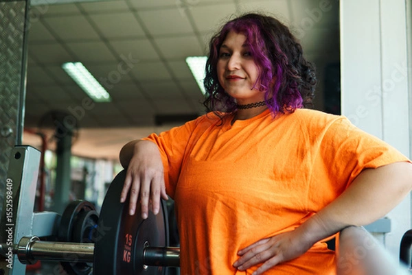 Fototapeta beautiful, overweight young latina posing happily and preparing to lift weights in a gym. positive, pushing herself to the limit. improvement and well-being.