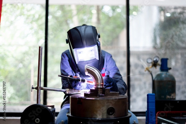 Fototapeta skilled indian worker working on welding machine on metal pipe in a workshop 