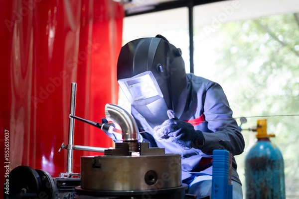 Fototapeta welder working with TIG welding machine on metal pipe in a workshop. Industrial setting with safety gear and precision engineering