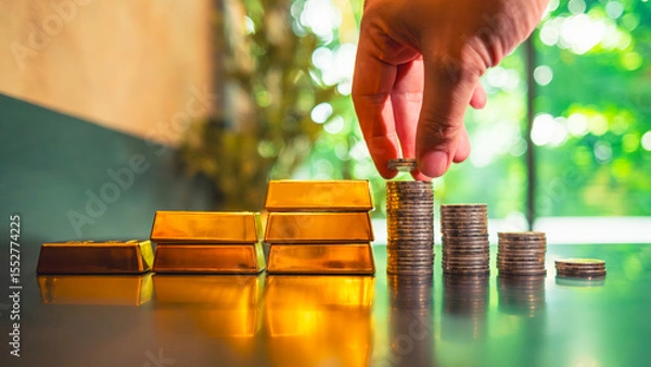 Fototapeta Investors are considering investing in gold by accumulating gold coins and stacking them higher and higher, with a pile of gold beside them. They view gold as the safest asset for investment.