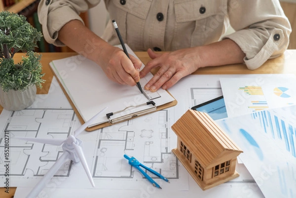 Fototapeta Engineer drawing blueprints for a sustainable house powered by a wind turbine, promoting renewable energy and ecological future
