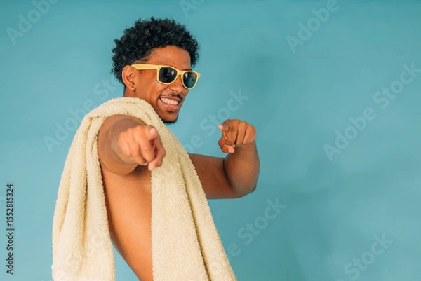 Obraz young latin man smiling with sunglasses and towel in swimsuit isolated on background, summer