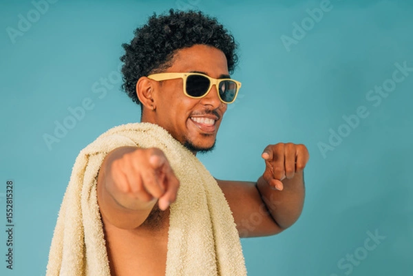 Obraz young latin man smiling with sunglasses and towel in swimsuit isolated on background, summer
