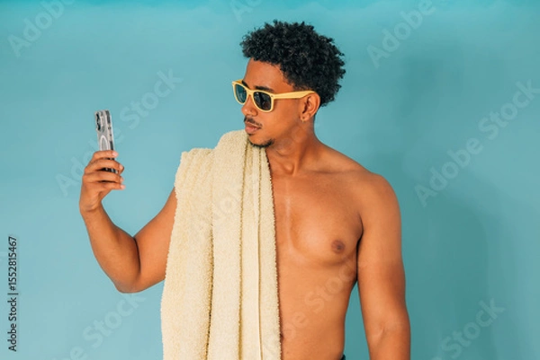 Obraz young latino man shouting, wearing sunglasses and a towel, isolated on white background, looking at his phone