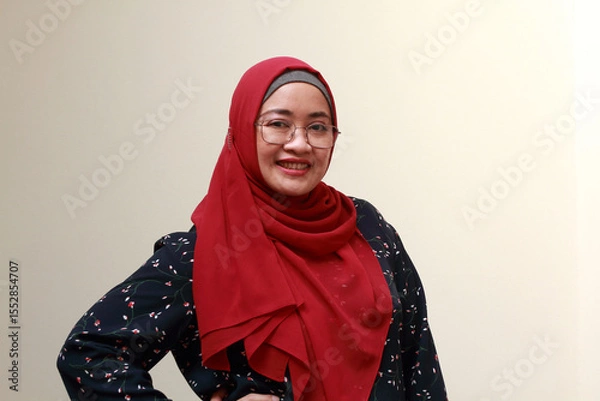 Fototapeta An Asian Muslim lady standing with one hand on her waist and smiling. Confidence expression.