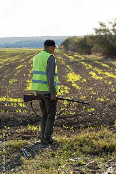 Fototapeta Mature man hunter with gun while walking on field.