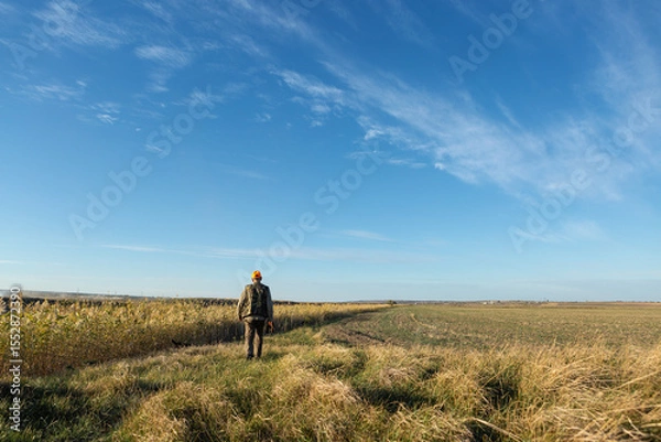 Fototapeta Mature man hunter with gun while walking on field.