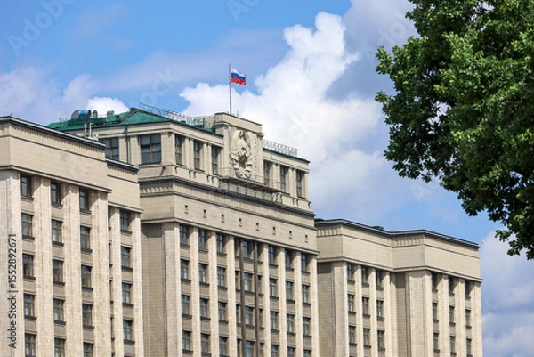 Fototapeta Parliament building with Russian flag in Moscow. The State Duma facade, view through the branches of summer tree