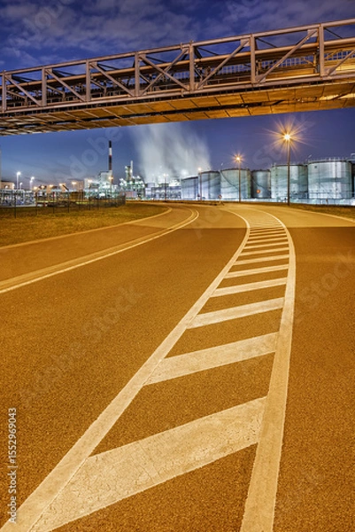 Obraz Bending road with road markings with illuminated oil refinery and storage tanks on background at night, port of Antwerp
