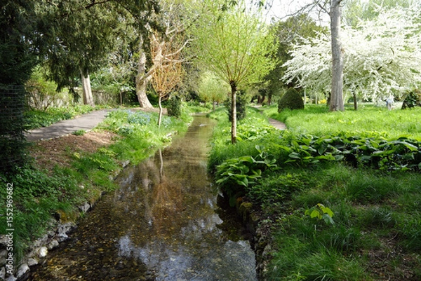 Fototapeta Peaceful stream flowing through vibrant spring garden with fresh greenery and blooming trees