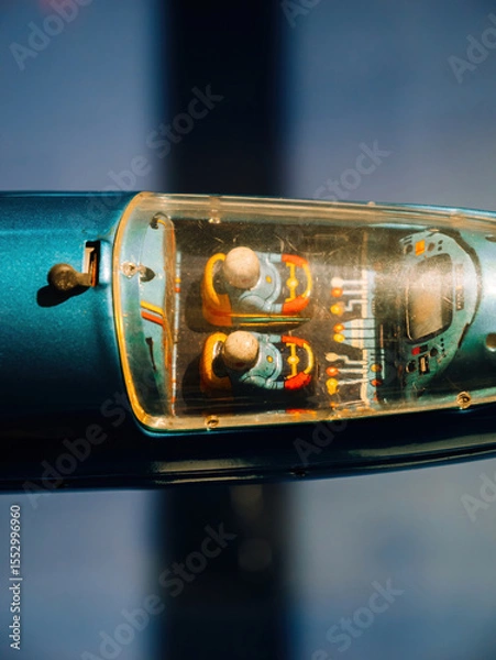 Fototapeta Close-up of a vintage toy vehicle cockpit with two illustrated robot pilots under a transparent plastic canopy, showcasing retro colors and mechanical interior details