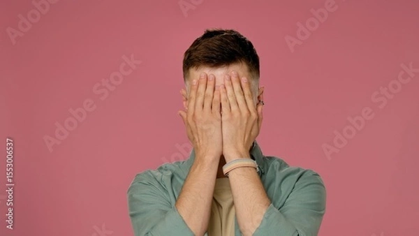 Fototapeta Man Hiding Face with Hands on Pink Background in Studio Setting