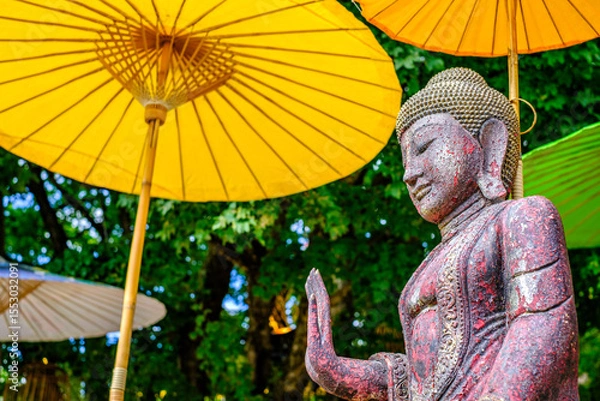 Fototapeta Serene Buddha statue under colorful parasols in a tranquil garden setting during a sunny afternoon