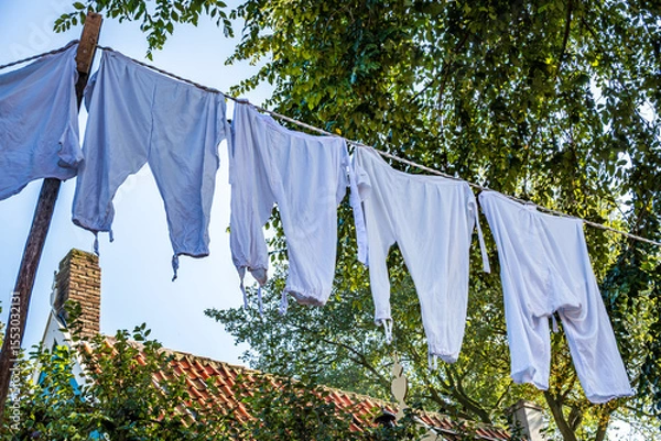 Fototapeta Colorful clothes drying on a line amidst lush green grass in a rural area during bright daytime