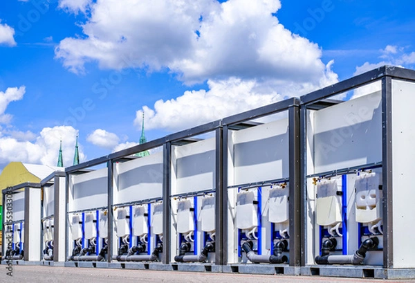 Fototapeta Portable restroom facilities lined up in a construction area under a blue sky with scattered clouds during daytime hours