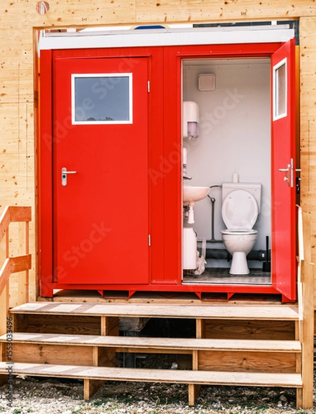 Fototapeta Portable restroom facilities lined up in a construction area under a blue sky with scattered clouds during daytime hours
