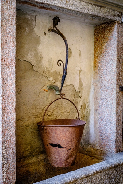 Fototapeta Historical stone fountain against a rustic wall in an Italian village, showcasing intricate craftsmanship and timeless charm in a serene setting