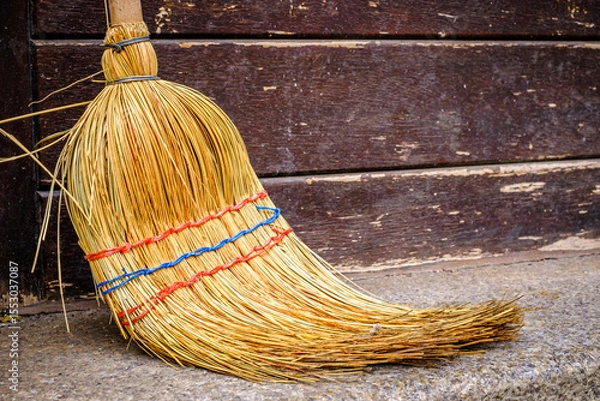 Fototapeta Traditional straw broom rests against a wooden shelf in a rustic setting during afternoon light