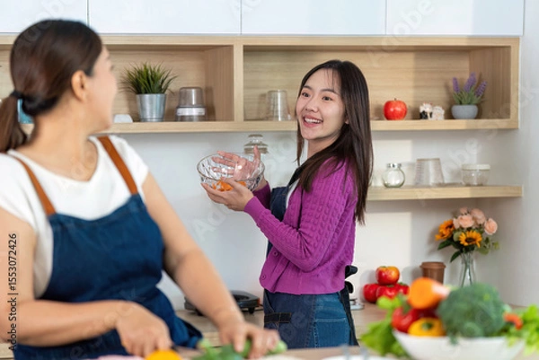 Obraz Cooking Together and Healthy Meal Prep. Two women laughing while preparing vegetables in a modern kitchen.