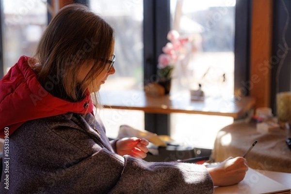 Fototapeta A talented artist captures her inspiration in a warm cafe, enjoying the sunlight and tranquility of the afternoon.
