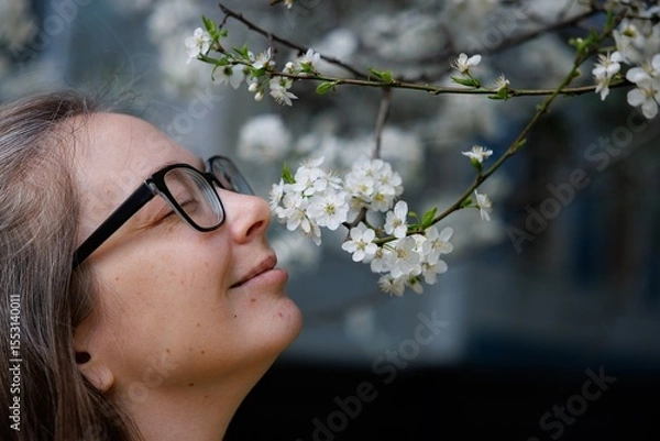 Fototapeta A woman joyfully engages with delicate blossoms, savoring the fragrant air while basking in springs warmth.