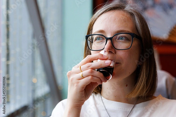 Fototapeta Savoring a rich drink while gazing thoughtfully out the window in a stylish city cafe setting.