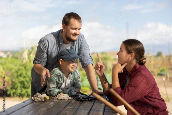 Fototapeta Family of farmers has fun talking at a wooden table after work. Farmers rest after planting seeds and cultivating the land.