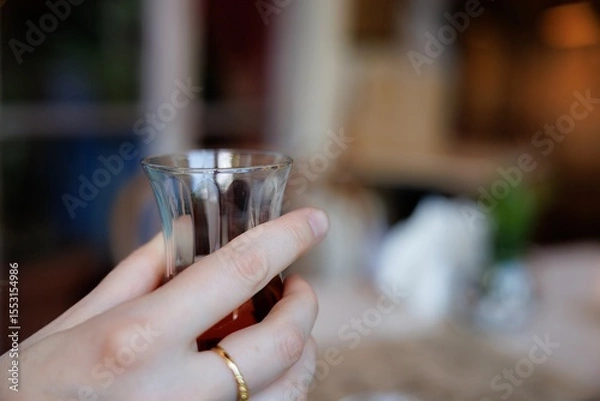Fototapeta A hand delicately holds a glass of tea, capturing the essence of relaxation in a charming cafe atmosphere.