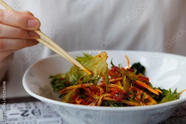 Fototapeta Hands delicately grasp chopsticks, picking up a colorful mix of fresh vegetables in a lively dining atmosphere.