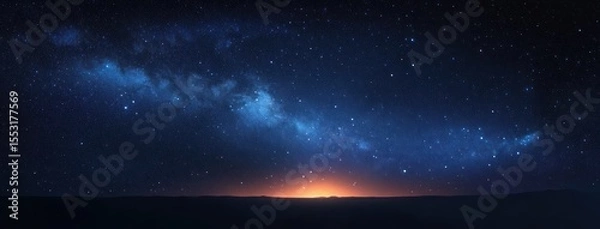 Fototapeta Vast night sky filled with stars and the glowing band of the Milky Way galaxy arching over a dark horizon with a soft warm light glow