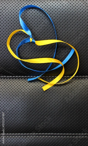 Obraz A symbolic heart made of yellow and blue ribbons in the colors of the Ukrainian flag on a black leather background. Vertical image with colored ribbons
