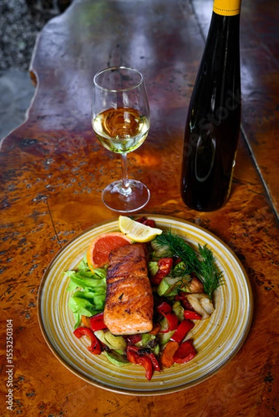 Fototapeta Baked salmon garnished with lemon, pepper and tomatoes with herbs and with a bottle and a glass of wine