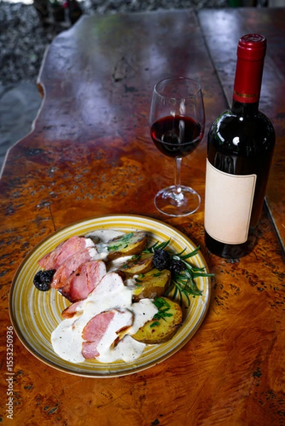 Fototapeta Pork fillet with potatoes and sauce wwith a bottle and a glass of wine