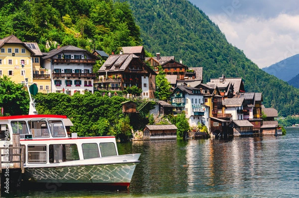 Fototapeta Hallstadt in Austria. A boat is docked in front of a house. The house is surrounded by trees and has a green roof