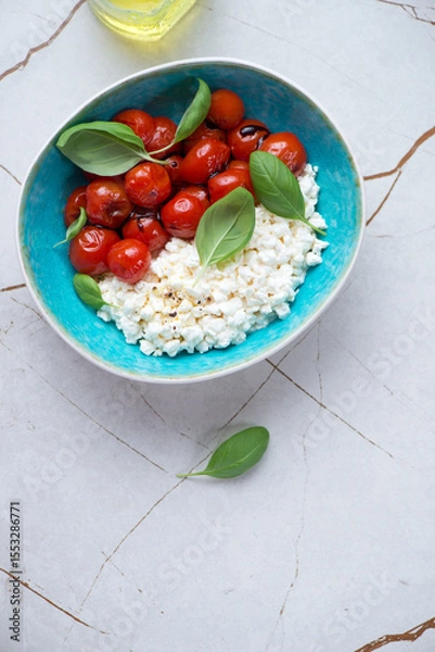 Fototapeta Cottage cheese caprese with roasted tomatoes and green basil, vertical shot on a white stone background with space, top view