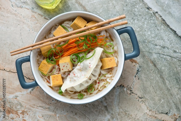 Fototapeta Rice noodles with smoked tofu and steamed dumpling, horizontal shot on a grey and roseate granite background, above view