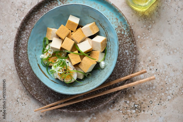 Fototapeta Smoked tofu cheese with marinated eggs in a turquoise bowl, horizontal shot on a beige granite background, top view